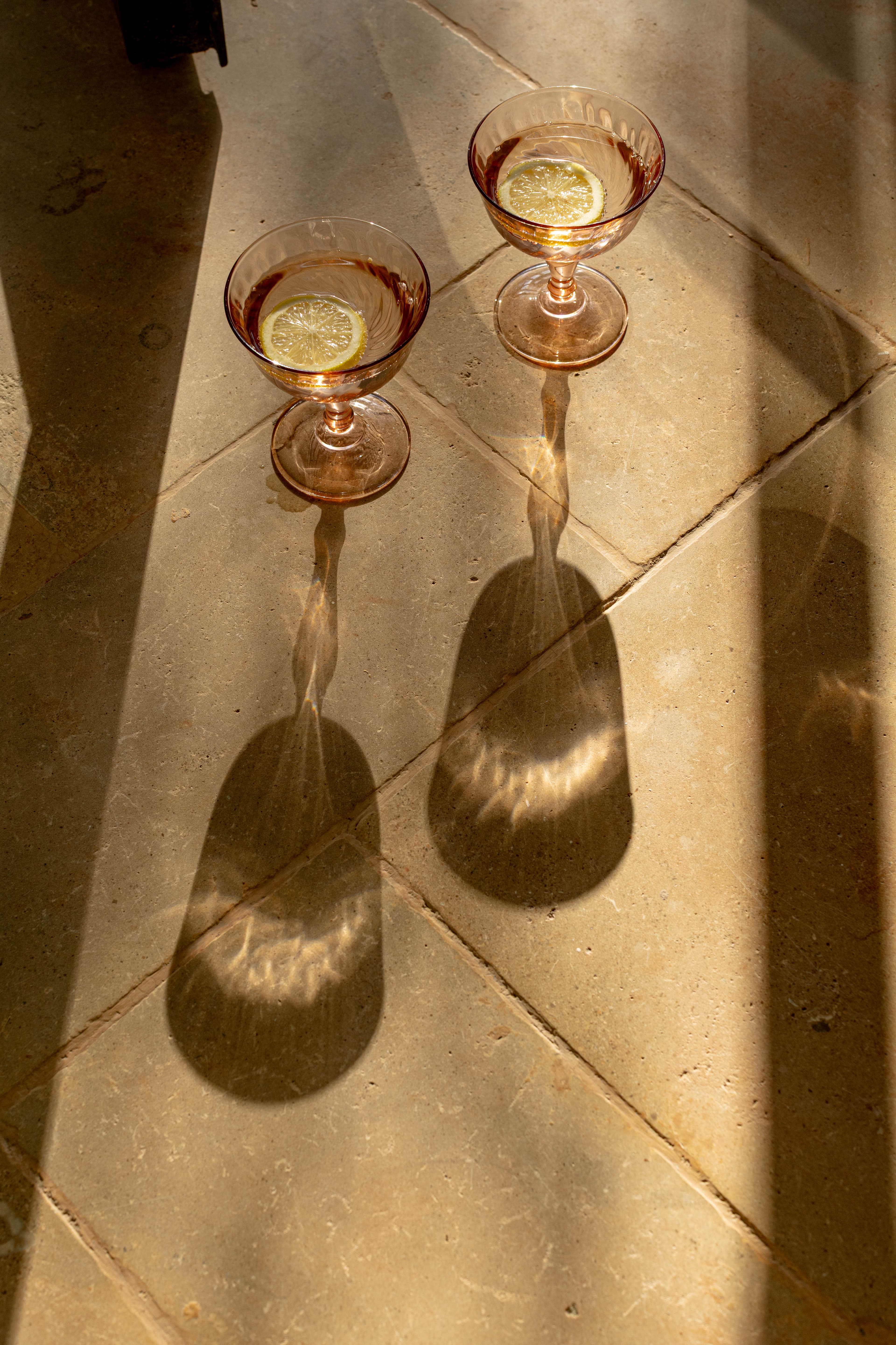 Deux coupes rosées au citron posées sur les dalles de pierre, longues ombres du soir