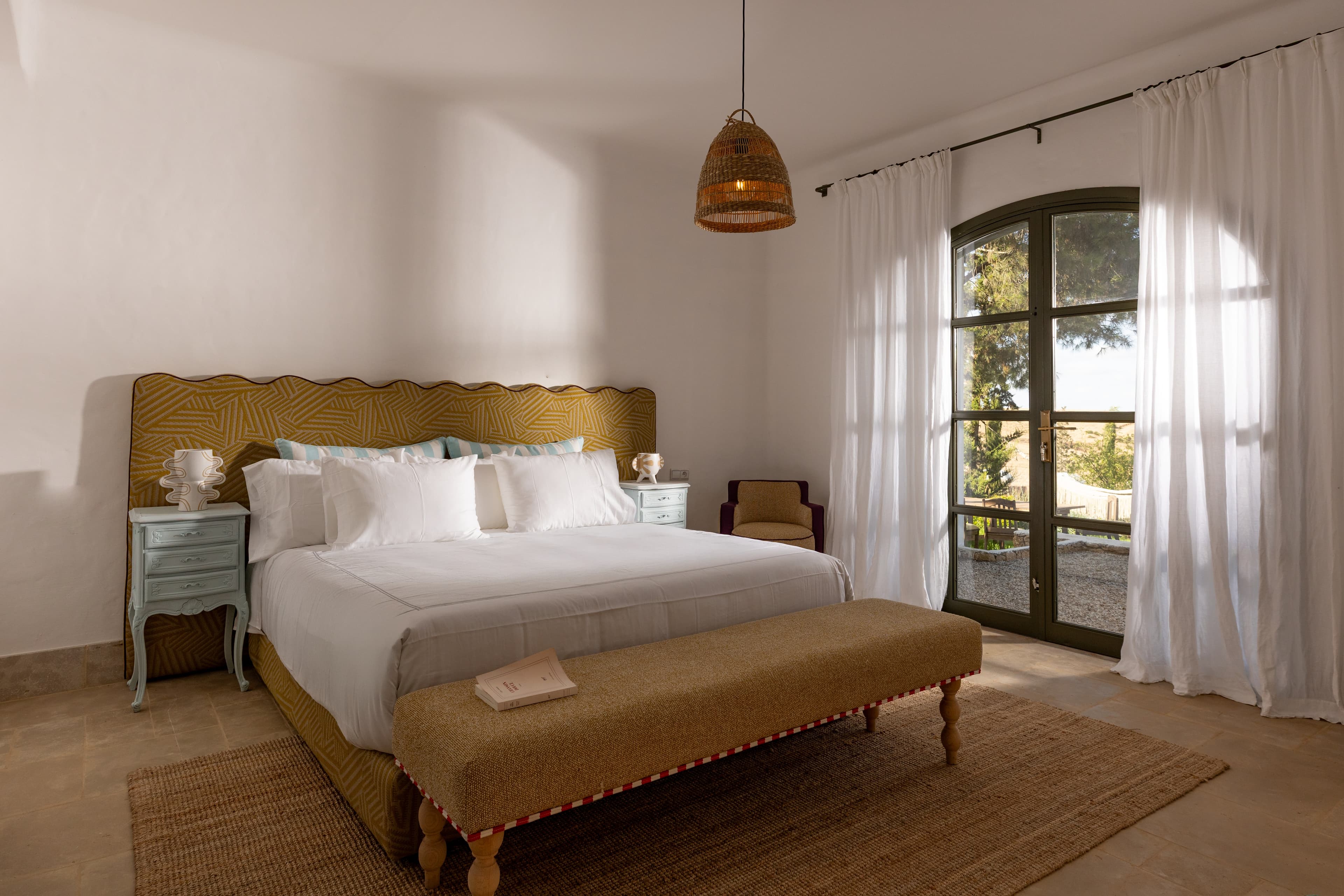 Chambre double à la tête de lit ocre graphique, voilages blancs et lumière du soir