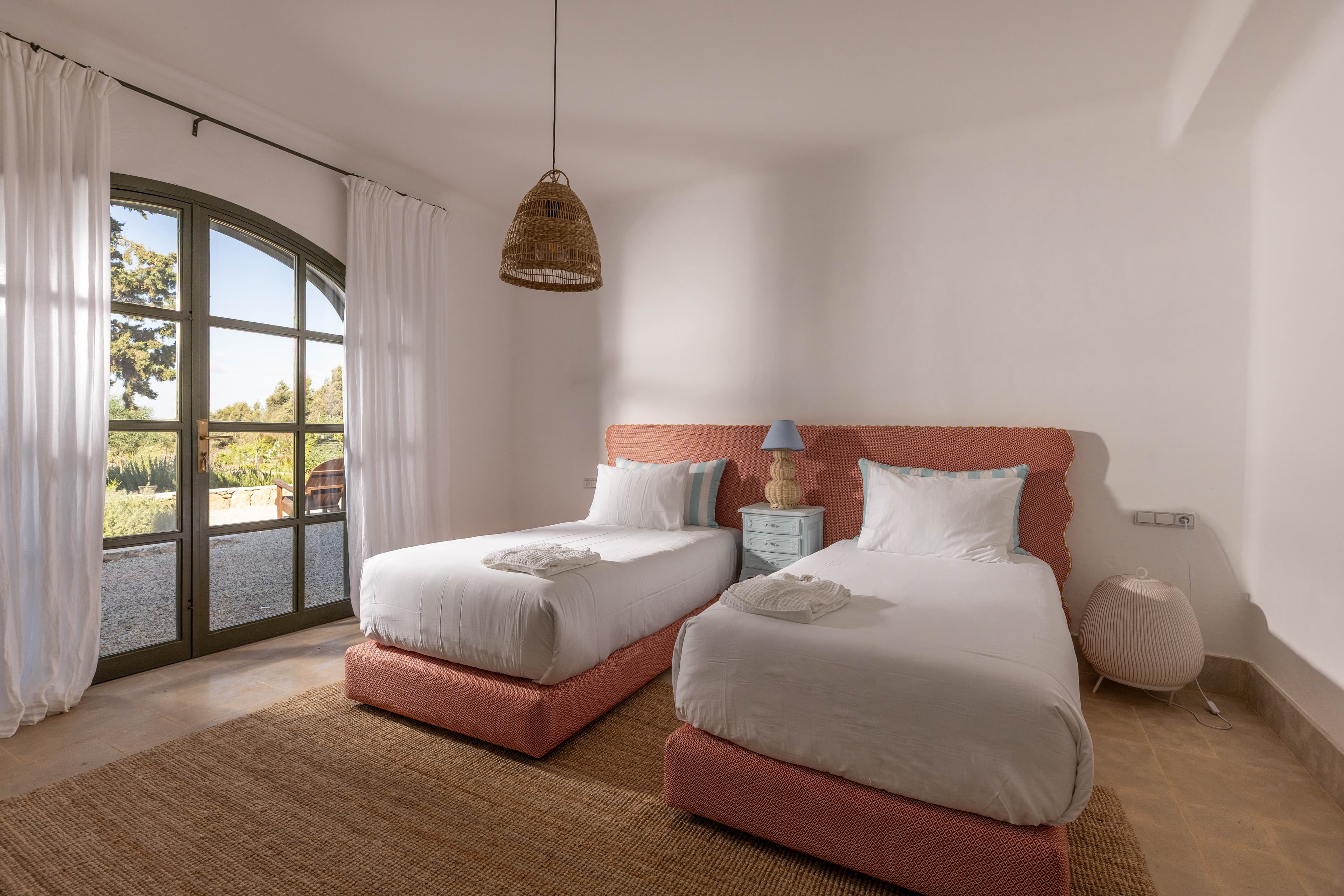 Chambre twin aux deux lits simples et tête de lit ondulée corail, ouverte sur le jardin