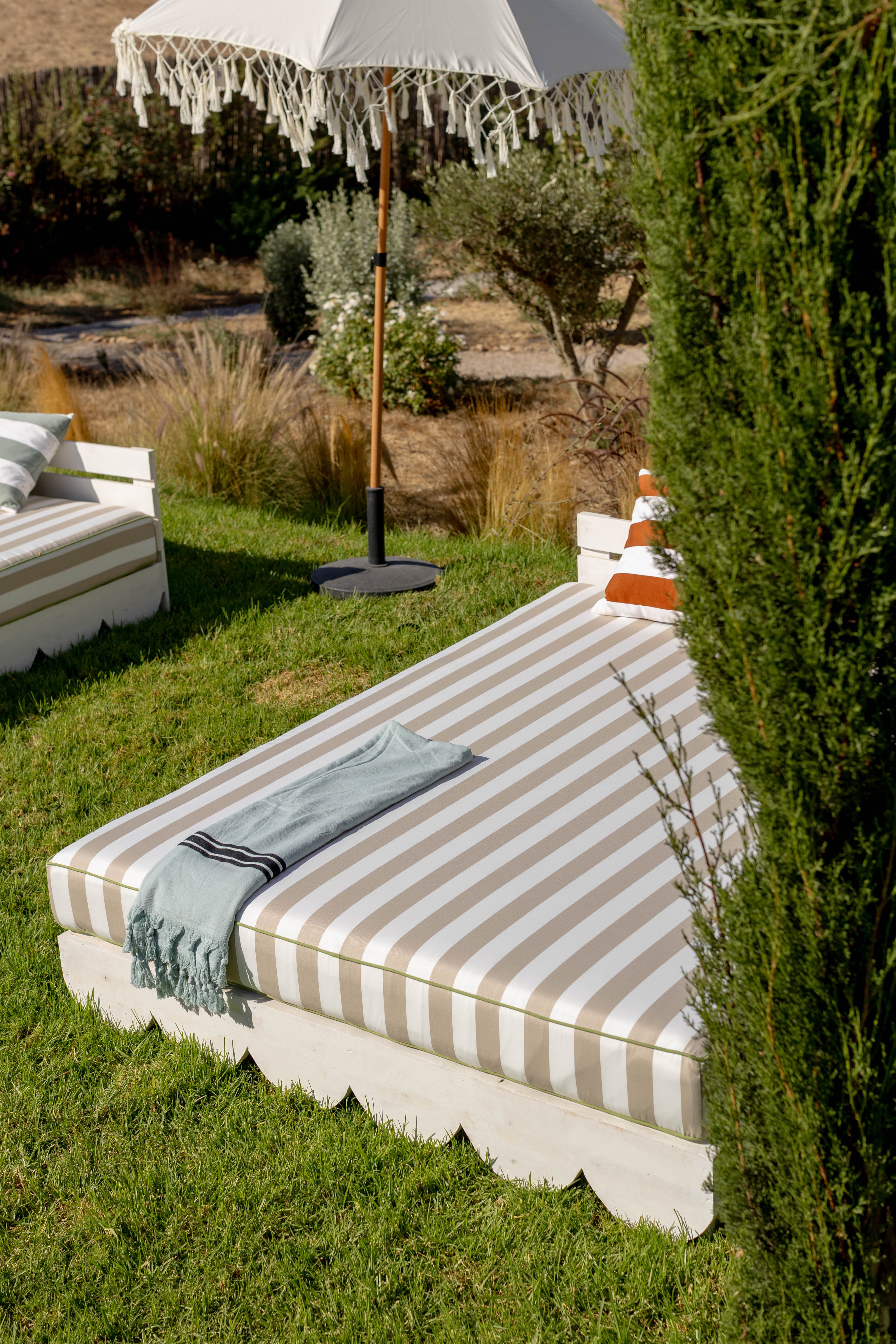Bain de soleil festonné à l'ombre d'un parasol à franges, entre les oliviers