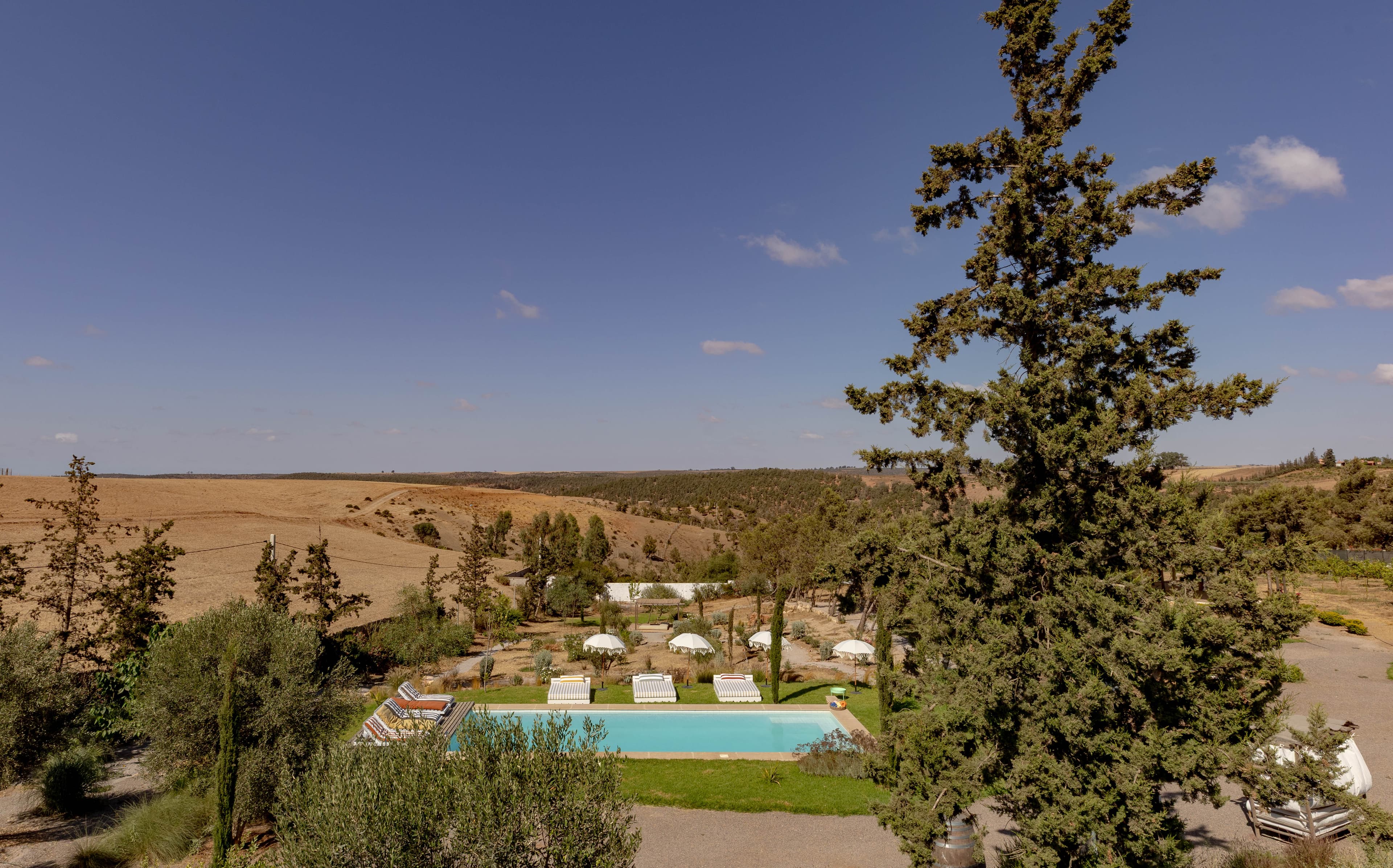 Le domaine vu d'en haut, piscine turquoise et parasols blancs au creux des collines dorées