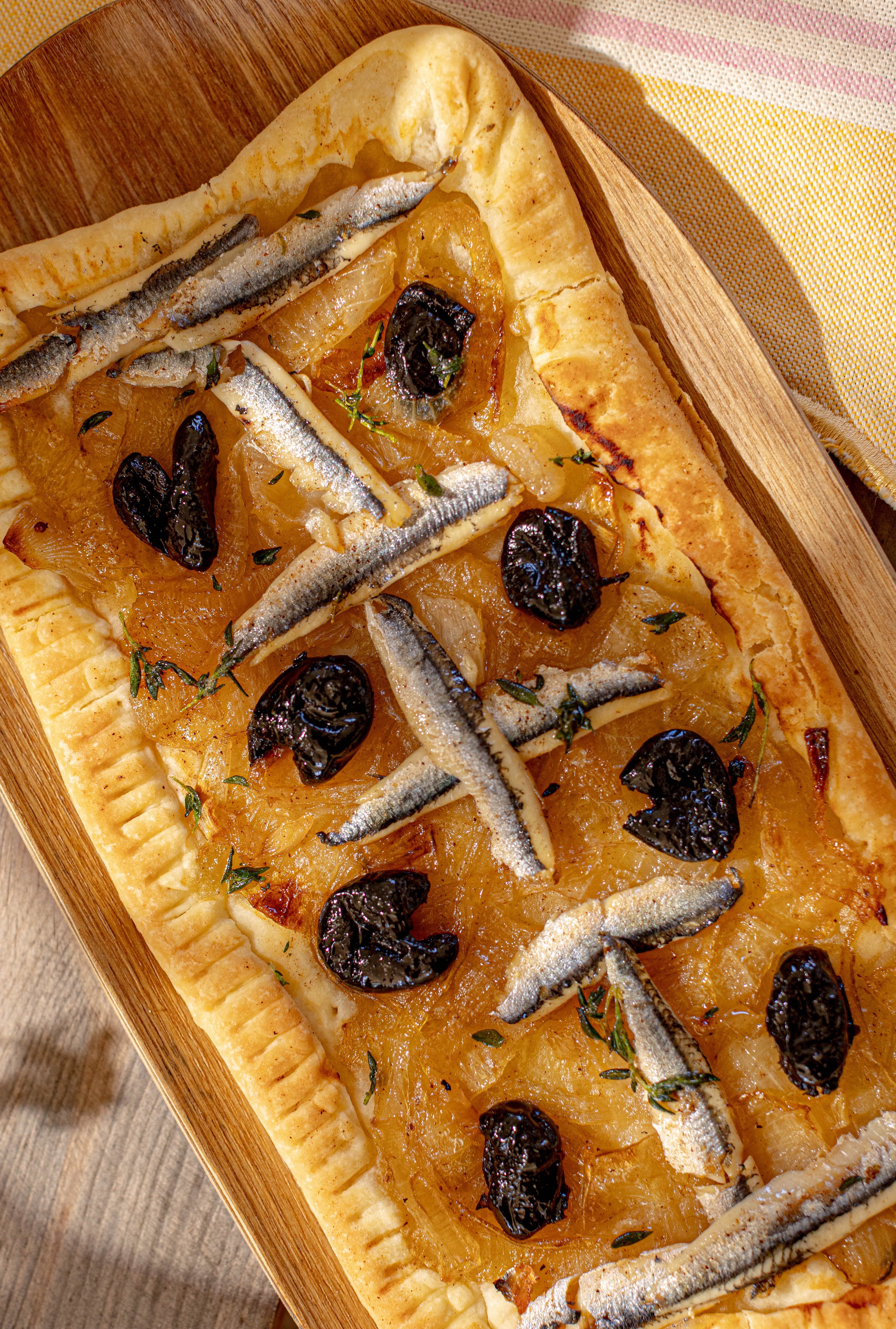 Focaccia aux anchois et aux olives sur sa planche, dans la lumière rasante